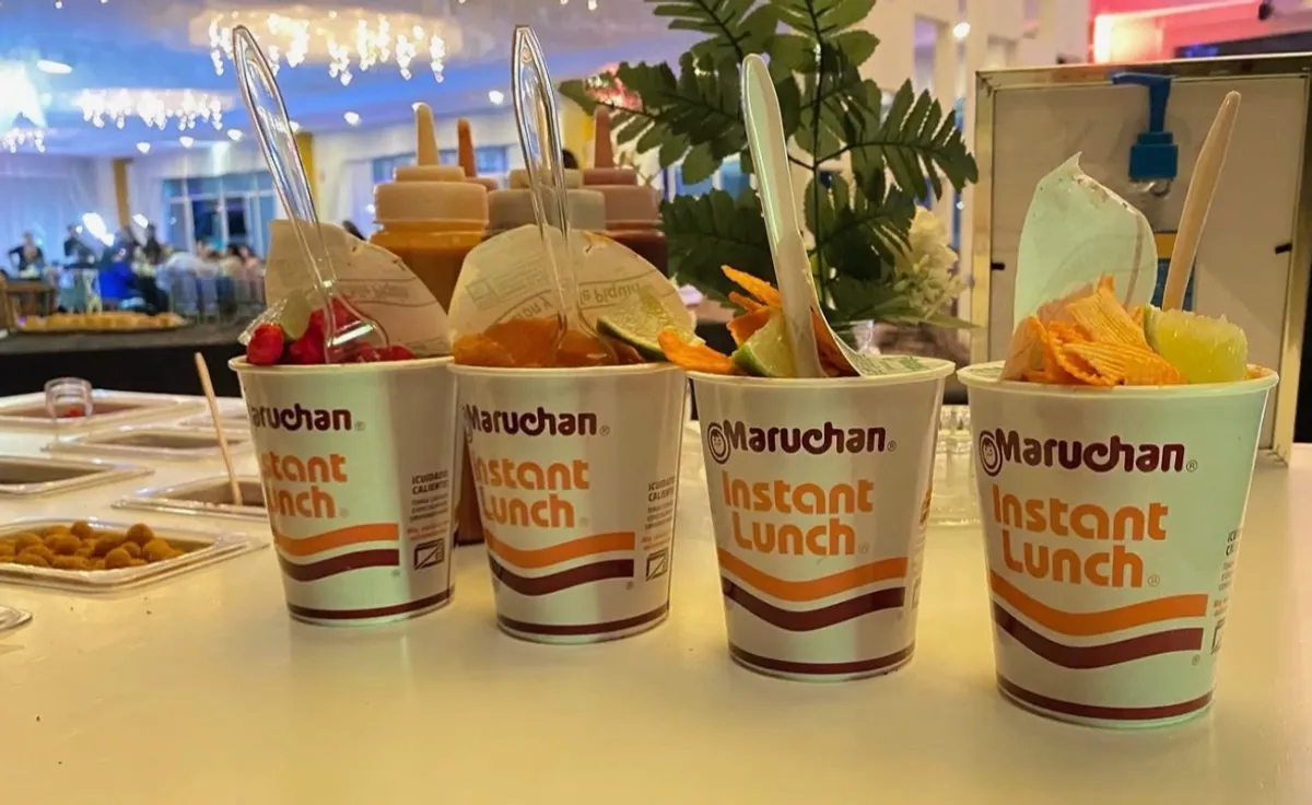 Maruchan instant lunch cups topped with chamoy, chips, and lime at an event